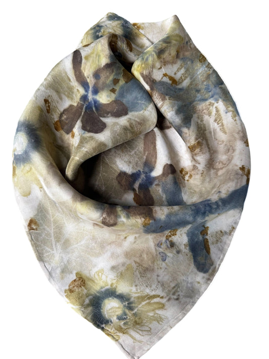 A square scarf with an abstract floral pattern in muted shades of blue, brown, and beige on a white background, styled in a loose knot against a plain white backdrop.